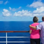 senior couple standing on the deck of a cruise ship looking at the ocean with their back on camera