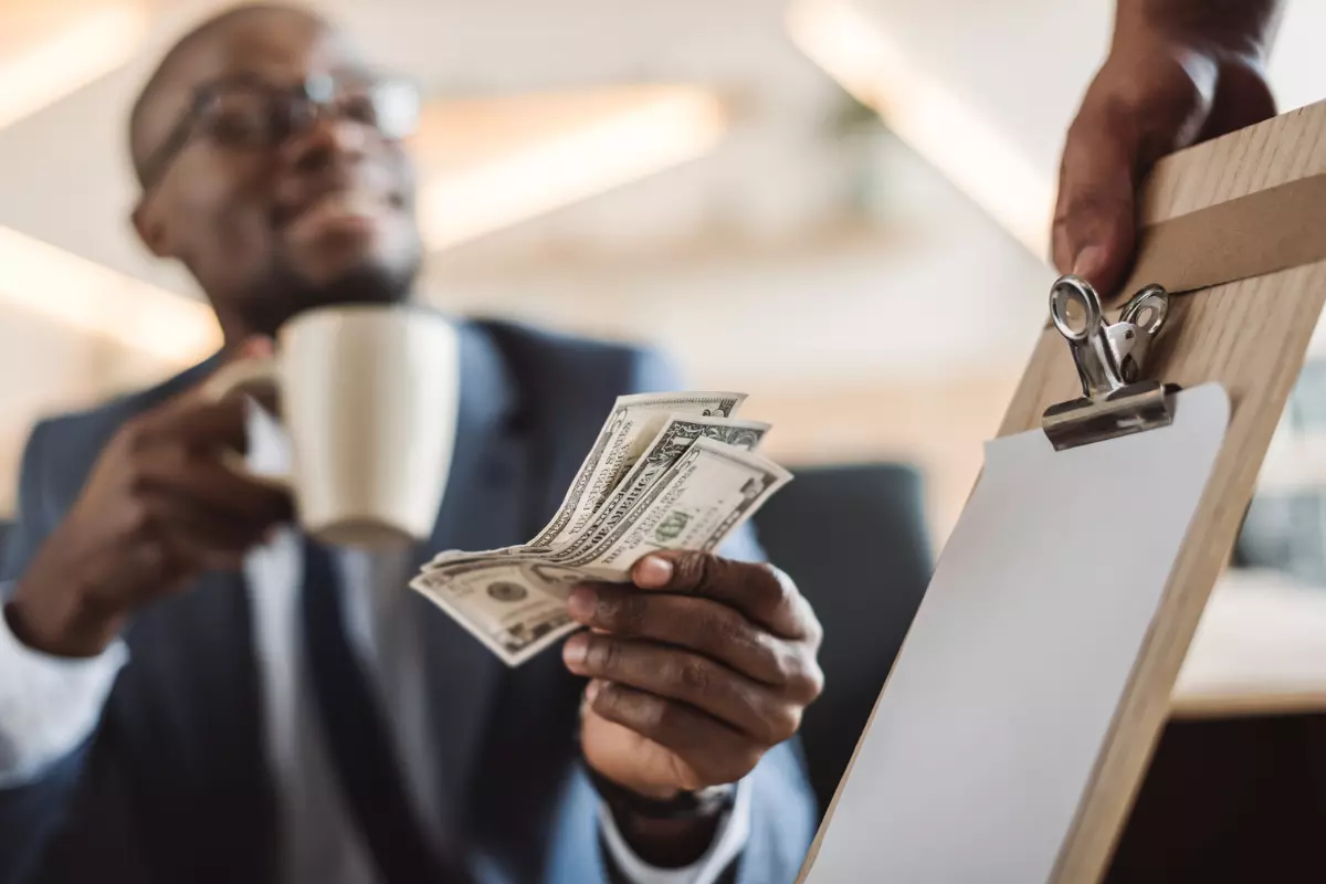 a black man paying a tip to the waiter holding a cup on hand.