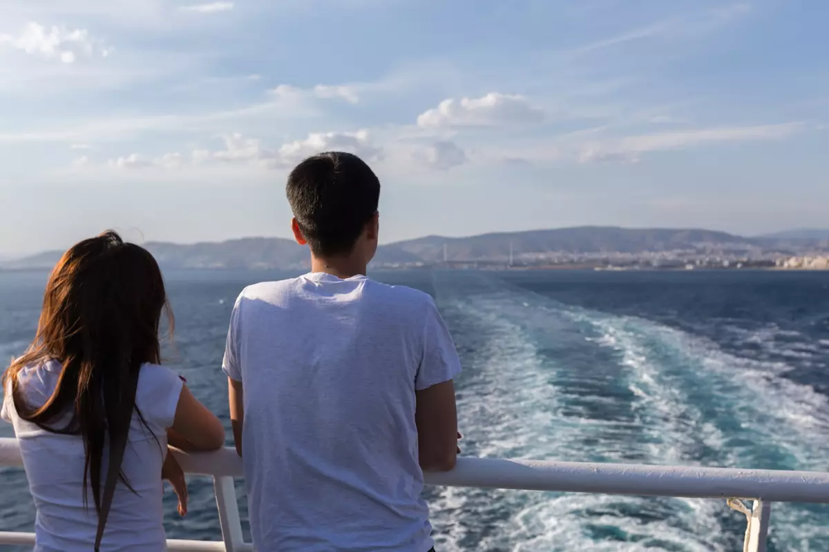 a couple standing at the back of a cruise ship watching the wake of the ship